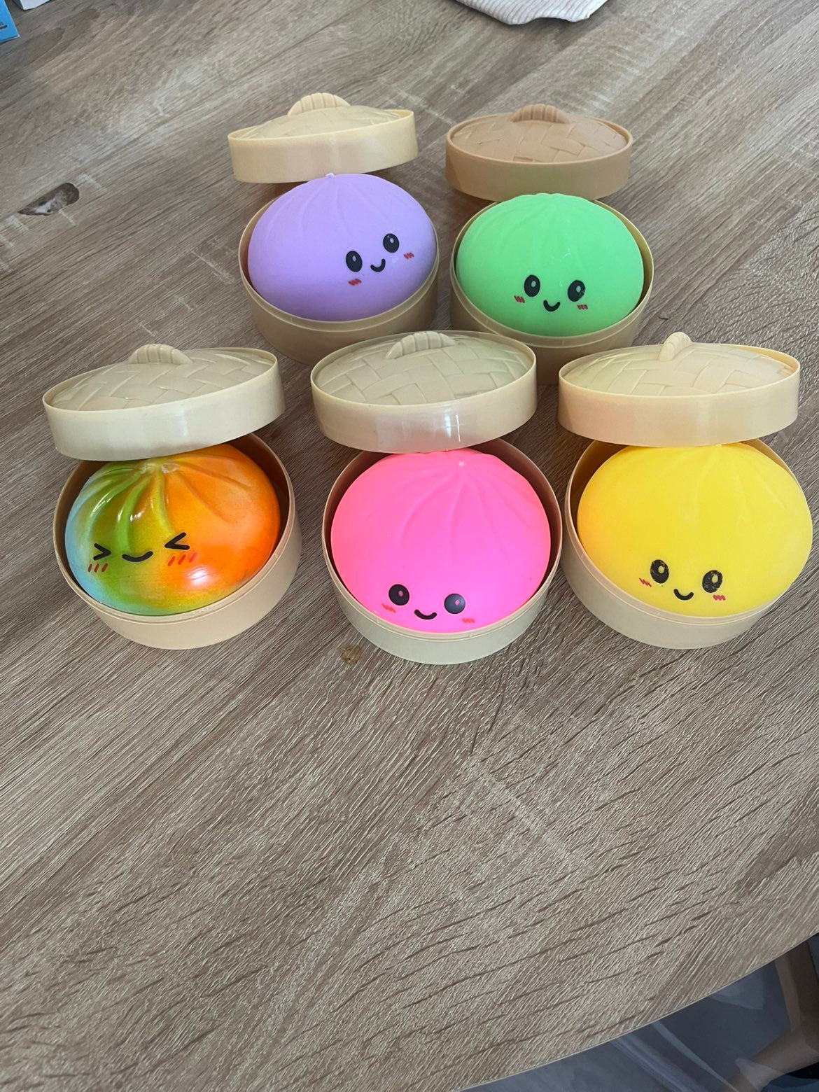 Six squishys bao colorés installés dans leurs paniers vapeur : violet, vert, orange dégradé, rose et jaune